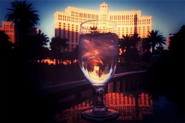 A glass of iced drink on a table reflects a luxury resort at sunset. Palm trees are visible in the background. Great for themes on relaxation, luxury vacations, serene getaways, and travel promotions.