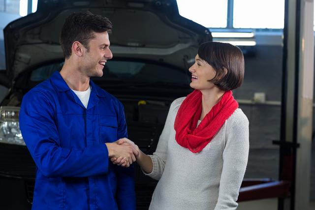Satisfied customer shaking hands with mechanic in repair garage
