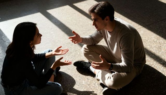 Young couple sitting cross-legged talking in sunlit room with terrazzo shadows
