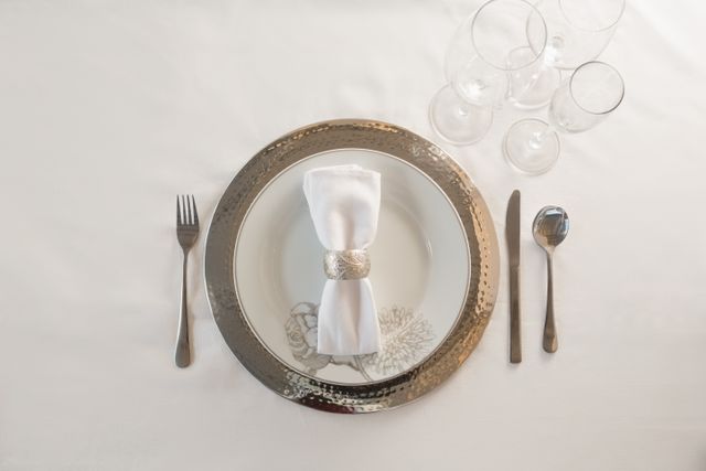 Elegant table setting featuring silverware, a neatly folded napkin with a decorative ring, and multiple glasses on a white background. Ideal for use in articles or advertisements related to fine dining, formal events, wedding receptions, or luxury dining experiences.