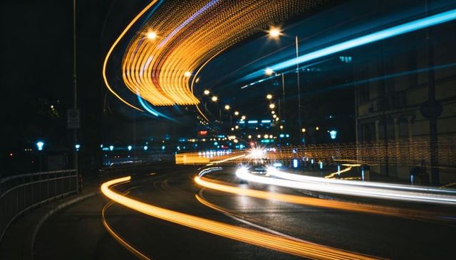 Curved neon light trails sweeping through night cityscape, long exposure motion and speed