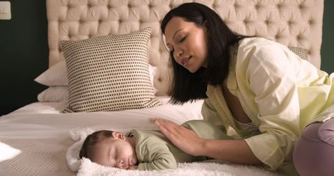 Asian Mother Soothing Sleeping Infant in Comfortable Bedroom