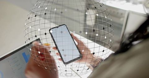 Holding smartphone while reviewing laptop analytics with digital globe network overlay