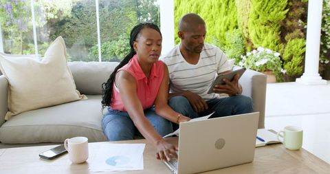 Couple Analyzing Finances Together Using Laptop and Tablet at Home