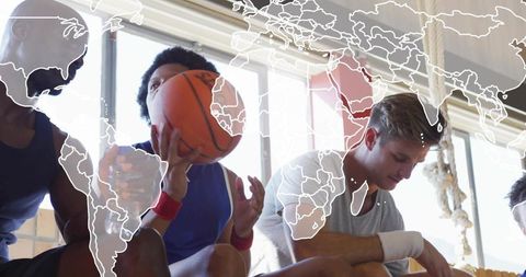 Basketball teammates resting and talking on bench with world map overlay in backlit gym