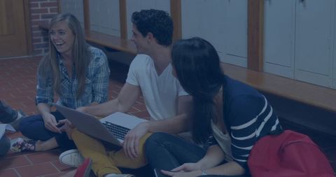 Laughing students collaborating on laptop in school hallway, sharing ideas and phones