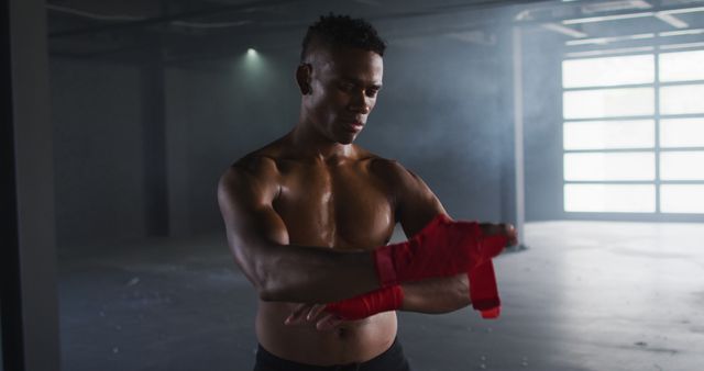 Shirtless african american man wrapping hands for boxing in an empty urban building. urban fitness, sport and healthy lifestyle.
