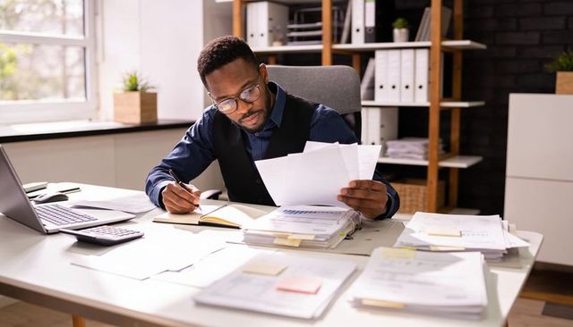 Focused businessman reviewing financial documents and taking notes at bright office desk