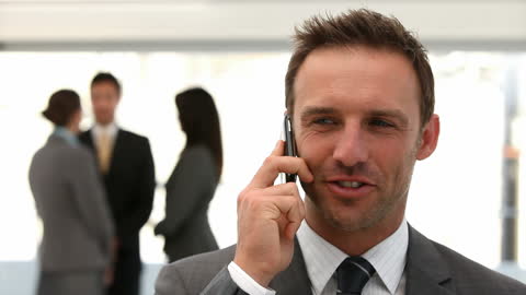 Confident Businessman Talking on Phone with Colleagues in Background