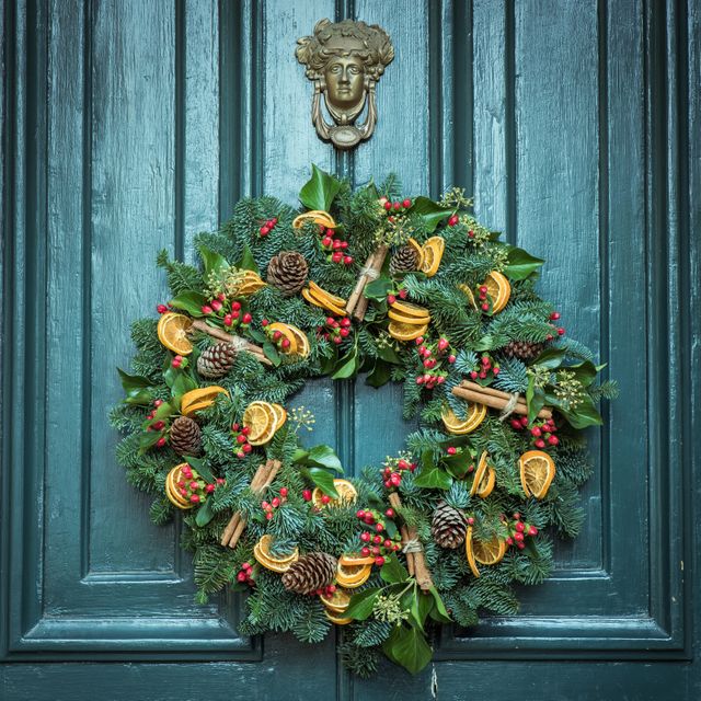 Traditional holiday wreath hanging on blue door, featuring pinecones, dried oranges, berries, and cinnamon sticks. Ideal for seasonal decor inspiration, holiday decoration ideas, or winter-themed postcards. Suitable for home decor literature, festive advertisement campaigns, or social media posts celebrating the Christmas season.