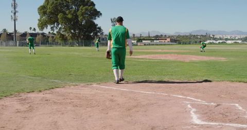 Baseball Player Walking Toward Pitcher's Mound on Sunny Neighborhood Field with Teammates