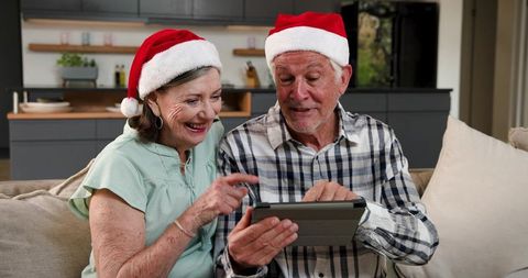 Joyful Senior Couple Using Tablet Wearing Santa Hats