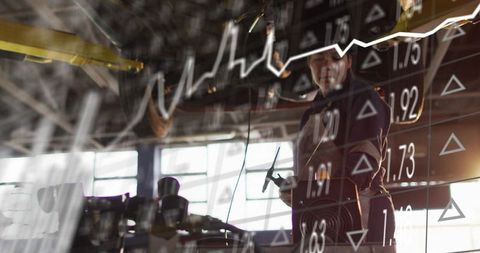 Industrial technician working in workshop with stock market data overlay showing growth trend