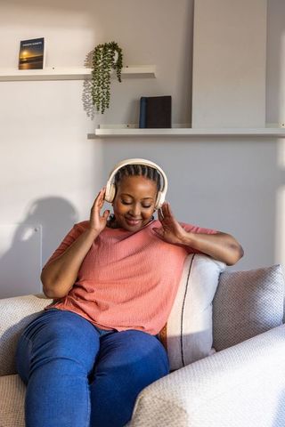 African american woman relaxing on sofa listening to music with wireless headphones