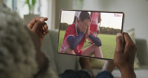Man Watching Soccer Game on Tablet Screen in Living Room