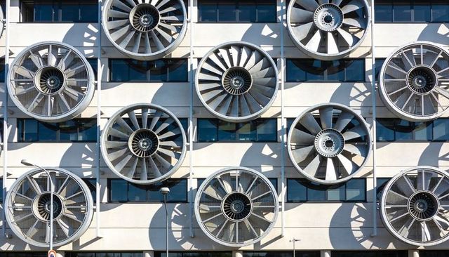 Urban facade featuring grid of giant industrial ventilation fans casting geometric shadows