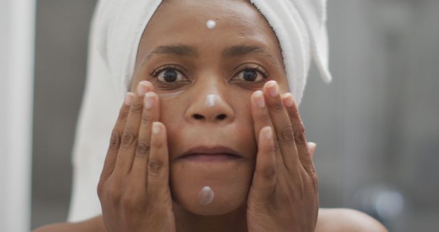 Happy african american woman apply cream on face in bathroom. domestic lifestyle, spending free time at home.