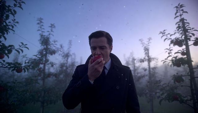 Gentleman biting red apple in misty orchard at dawn wearing trench coat and tie