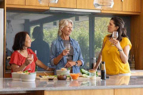 Women gathering in sunlit modern kitchen holding wine glasses and sharing conversation