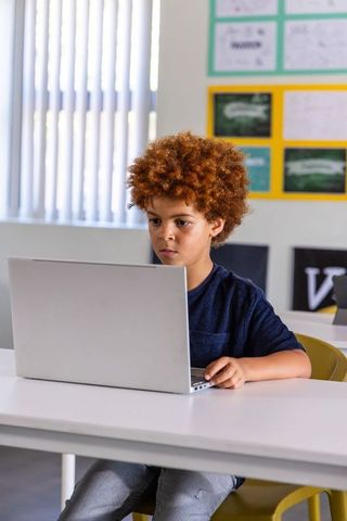 Focused African American Boy Working on Laptop in Bright Classroom for Digital Learning