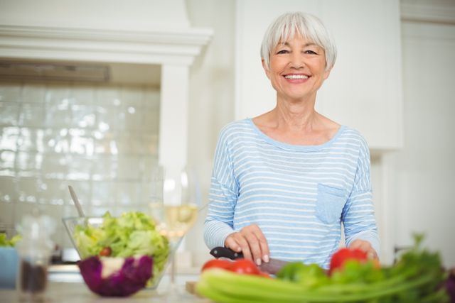 Portrait of senior woman preparing vegetable salad in kitchen