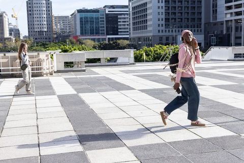 Woman in pink hoodie walking across urban rooftop listening to music with smartphone