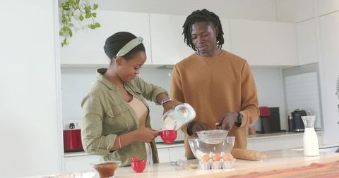 African american couple baking together in bright modern kitchen mixing and sifting ingredients