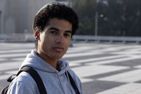 African american teen standing in urban plaza wearing grey hoodie and backpack