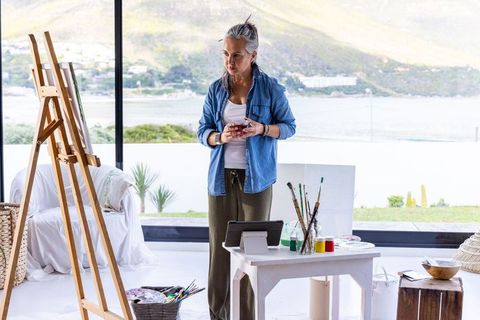 Senior woman painting in bright coastal studio creating canvas with natural light