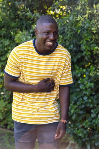African American man laughing in yellow striped tee showing wristwatch in garden