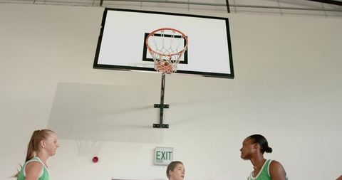 Diverse female basketball teammates calling plays under hoop on indoor gym court showcasing teamwork