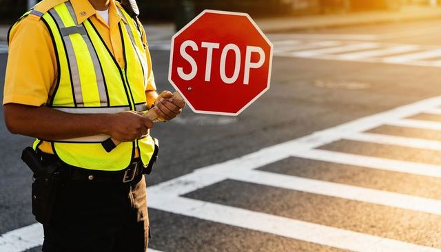 Crossing guard holding stop sign on crosswalk wearing high-visibility vest and duty belt