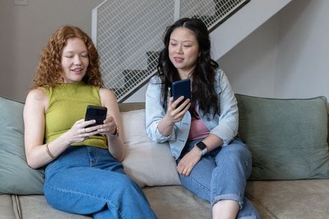 Diverse friends comparing smartphones on couch, casual home tech and social sharing