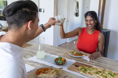African american couple clinking glasses during homemade curry dinner at wooden table happy