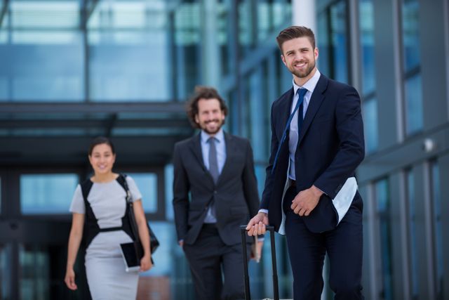 Business professionals walking with luggage outside a modern office building. Ideal for use in corporate websites, business travel promotions, teamwork and collaboration themes, and professional services advertisements.