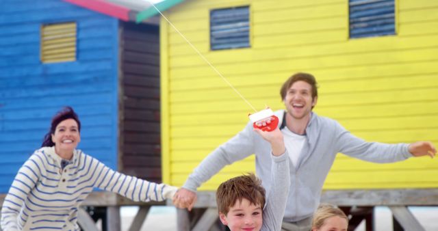 Happy Family flying Kite at Beach Near Colorful Cabins - Download Free Stock Images Pikwizard.com