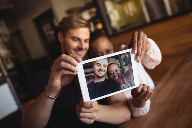 Happy couple taking selfie from digital tablet in restaurant