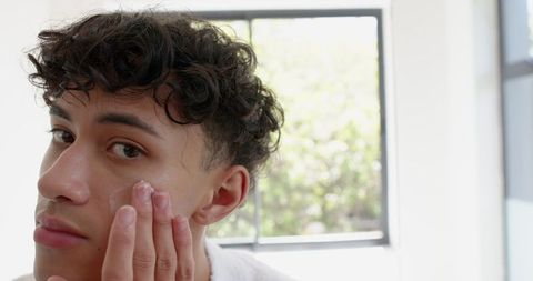 Man applying facial moisturizer in bright bathroom skincare routine