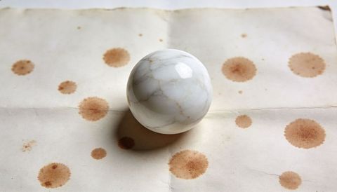 Polished veined marble sphere resting on aged paper with coffee stains, crease and soft shadow