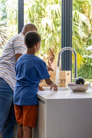 African american father and son washing hands at modern kitchen island with garden view
