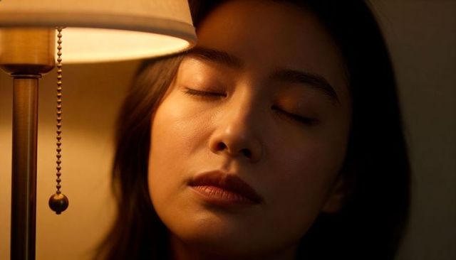 Serene woman resting in warm bedside lamp glow, intimate closeup portrait with pull-chain