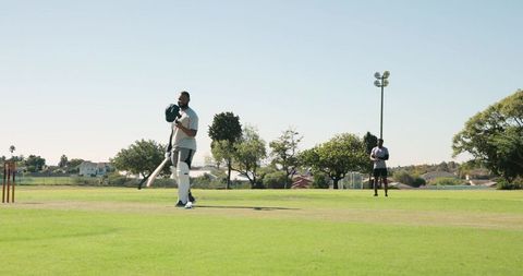Batsman swinging bat on suburban cricket pitch in park near wooden stumps