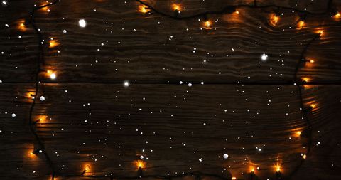 Snow Falling on Fairy Lights and Wooden Background