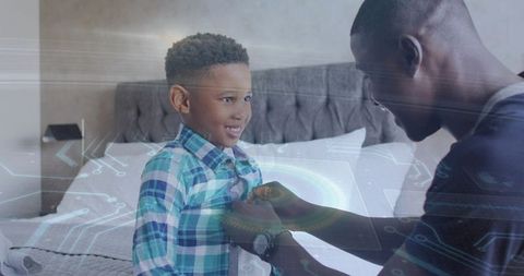 Father fastening shirt for smiling son on bed with futuristic hud overlay, family bonding