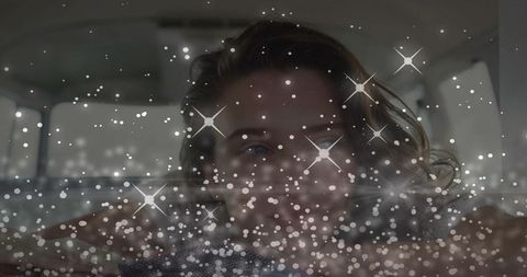 Smiling woman leaning in car backseat with sparkling bokeh star flare overlay