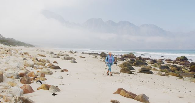 A senior hiker walks on a foggy beach with hiking poles, highlighting adventure and fitness. Useful for advertising retirement activities, exploring the great outdoors, promoting healthy living in senior age, travel brochures, or fitness guides.