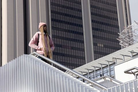 Urban portrait of african american man standing on white staircase in pink hoodie