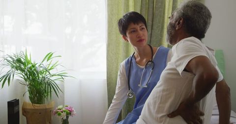 Senior Man with Back Pain Talking to Doctor in Retirement Home
