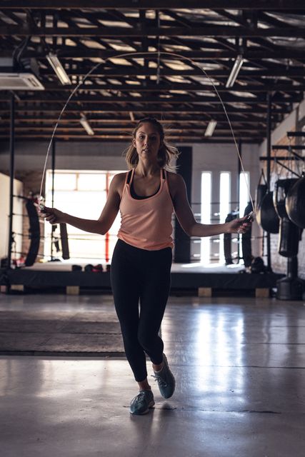 Young female boxer skipping rope in a gym. Ideal for use in fitness, sports, and health-related content. Perfect for promoting gym memberships, workout routines, and athletic apparel.