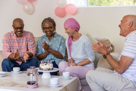 Senior Friends Celebrating Birthday with Cake and Balloons Indoors